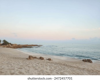 A serene beach at dusk with gentle waves, a rocky shoreline, and a pastel-colored sky creating a peaceful atmosphere. - Powered by Shutterstock