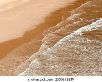 A serene beach scene captured from above, with gentle waves lapping against the soft, sandy shoreline. The gradient of wet and dry sand creates a beautiful contrast, as the foamy water meets beach. - Powered by Shutterstock