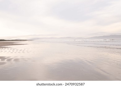 A serene beach scene featuring a calm shoreline, gentle waves, and a misty horizon. The tranquil ambiance is enhanced by soft, pastel skies, seascape, and relaxation themes. Focus at the coast view. - Powered by Shutterstock