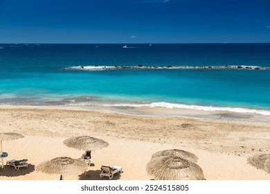 A serene beach scene at Playa del Duque, Tenerife with several sun loungers and straw parasols. Concept: beach holidays, leisure activities, and tourism in Tenerife - Powered by Shutterstock