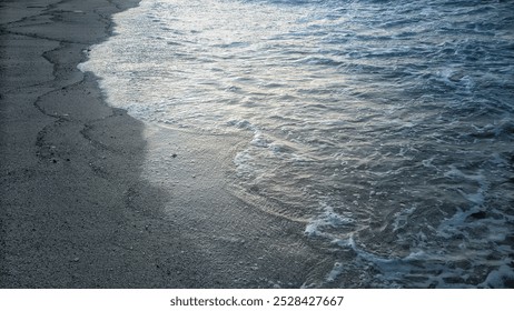 a serene beach scene with soft waves gently washing over a sandy shore. The water appears clear and light blue, gradually merging with the smooth sand as the tide flows in. - Powered by Shutterstock