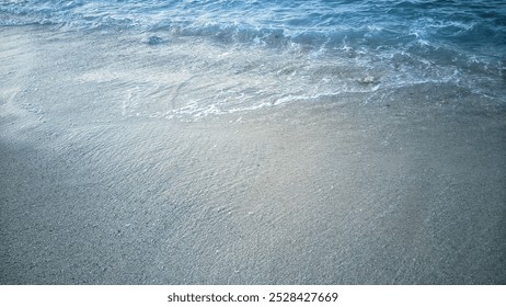 a serene beach scene with soft waves gently washing over a sandy shore. The water appears clear and light blue, gradually merging with the smooth sand as the tide flows in. - Powered by Shutterstock