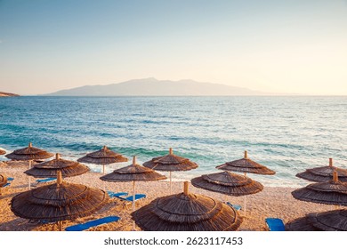 Playa serena al atardecer y filas de tumbonas con sombrillas con vistas a la tranquila costa. Lugar de Locación Saranda, Albania, Europa. Fondo de pantalla de fotos. Descubre la belleza de la tierra.