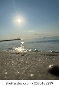 A serene beach view capturing sunlight reflecting off gentle waves. The sandy shore is in focus, while the distant pier and silhouettes of people create a peaceful ambiance.