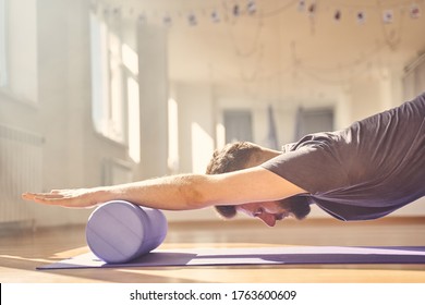 Serene bearded man placing hands on yoga roller block and meditating in yoga studio