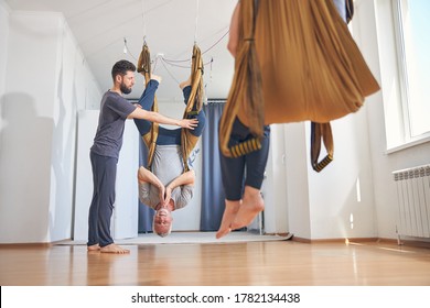 Serene beginner yogi in a silk hammock hanging upside down supported by his personal trainer - Powered by Shutterstock