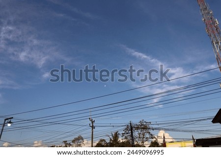 
A serene blue sky serves as a backdrop to a network of electrical cables, crisscrossing the horizon like veins of modern civilization, juxtaposing nature's vastness with human infrastructure.