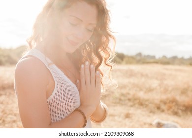 Serene boho woman with hands at heart center in sunny rural field