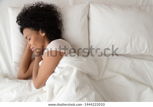 静かで落ち着いたアフリカ系の女性が寝心地の良いベッドで寝 柔らかい枕の整形外科用マットレスの上に寝 寝室の白いシーツの上に毛布で覆われた平和な若い黒い女性 トップビュー の写真素材 今すぐ編集