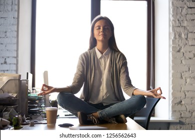 Serene Calm Business Woman Sit On Office Desk Taking Break For Meditation, Mindful Employee Doing Yoga Exercise In Lotus Pose For Relaxation At Workplace, No Stress Relief, Balance At Work Concept