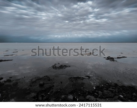A serene capture of the Rio de la Plata on a cloudy day, where the tranquil river mirrors the muted sky. The subtle blend of nature and cityscape creates a calm and contemplative atmosphere