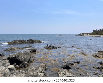 A serene coastal landscape featuring rocky shores, clear blue skies, and calm ocean waters, creating a peaceful and refreshing natural setting. - Powered by Shutterstock