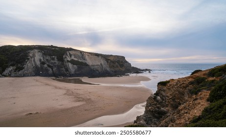 A serene coastal landscape featuring rugged cliffs and a sandy beach at sunset. The tranquil waters of the ocean gently meet the shoreline along the picturesque coastline of Portugal. - Powered by Shutterstock