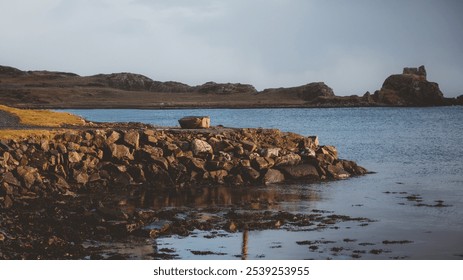 Serene coastal landscape with rocky shores, calm waters, and distant hills under a muted sky, creating a peaceful and natural scene perfect for travel inspiration - Powered by Shutterstock