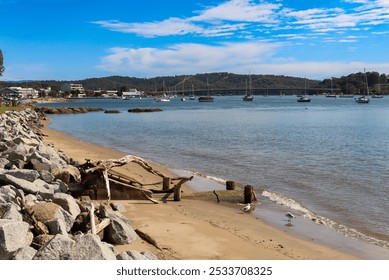 A serene coastal scene with boats anchored in a bay, rocky shoreline, and clear blue sky. - Powered by Shutterstock