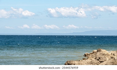 serene coastal view with calm turquoise waters lapping against rocky shores, and a distant mountain range. - Powered by Shutterstock