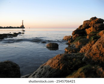 Serene coastal view with a lighthouse, rocky shore, and calm sea at sunset. Perfect tranquility. - Powered by Shutterstock