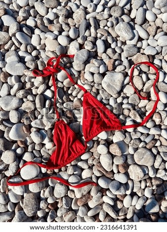 Serene Connection to Nature: Embracing Freedom, Spiritual Awakening through Nudist Exploration on the Beach, Red Bikini Top Rests on the Stones, Symbolizing Liberation and Authenticity of Nudist Life
