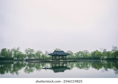 A serene dawn scene with a Korean traditional pavilion and trees reflected on the lake, surrounded by a gentle mist. - Powered by Shutterstock