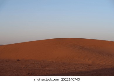 A serene desert scene featuring a large red sand dune under a bright blue sky, with subtle footprints visible on its surface and the dune casting a shadow. - Powered by Shutterstock