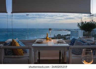 Serene dining setup for two on a balcony with a view of the Mediterranean Sea, a luxury hotel resort, lush greenery, and soft evening light.
