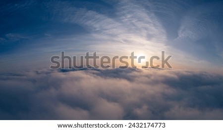 A serene drone view of the sun rising above a vast expanse of fluffy clouds.