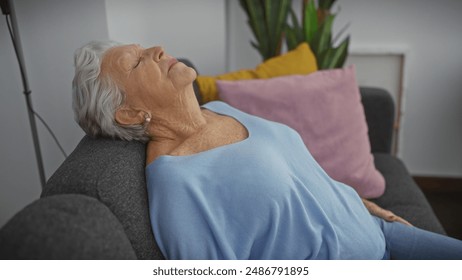 A serene elderly woman relaxes on a couch at home, eyes closed and a hint of a smile, exuding tranquility and comfort. - Powered by Shutterstock