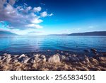 Serene Erhai Lake in Dali, Yunnan, China.  A picturesque view of calm waters, rocky shoreline, and mountains under a vibrant blue sky.