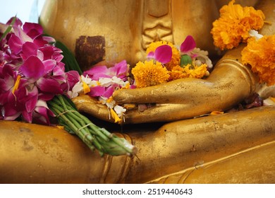 A serene golden Buddha statue adorned with vibrant floral offerings, showcasing a peaceful gesture that represents worship, tranquility, and devotion in a cultural setting. - Powered by Shutterstock