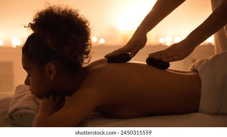 A serene image capturing a moment of relaxation, african american woman enjoys a hot stone therapy massage in a dimly lit spa setting The warmth and care are palpable - Powered by Shutterstock