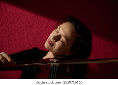 A serene image of a woman absorbed in playing the violin, eyes closed, against a vibrant red textured background. - Powered by Shutterstock