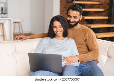 Serene Indian couple spending time together at home, using laptop for online shopping, web browsing, ethnic young wife and husband resting on the sofa in modern apartment, watching movie together - Powered by Shutterstock