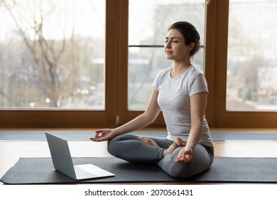 Serene Indian ethnicity woman sit cross-legged on yoga mat listen soothing music on laptop, do meditation practise with eyes closed alone indoor. Remote e coach training, modern tech, work out concept - Shutterstock ID 2070561431