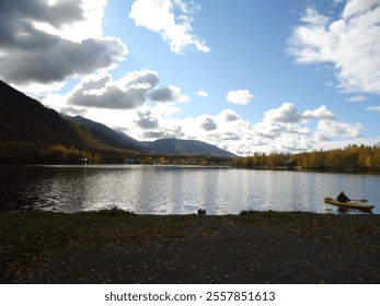 Serene lake with mountains, cloudy sky, and a person kayaking on calm waters. - Powered by Shutterstock