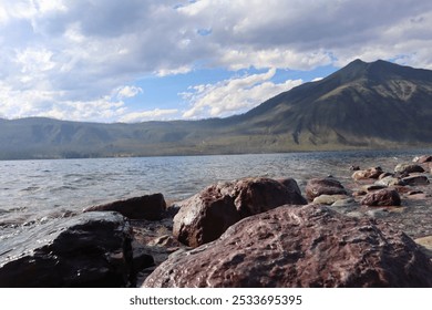 A serene lake with rocky shore and mountain backdrop under a partly cloudy sky, perfect for nature and travel themes. - Powered by Shutterstock