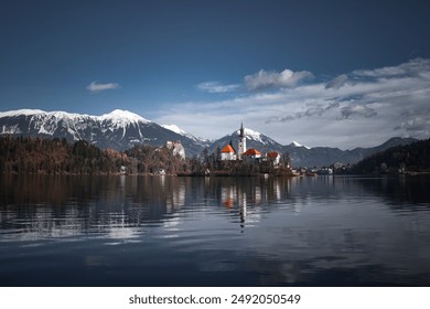 a serene lake with a small island featuring a church, set against snow-capped mountains and a clear sky. - Powered by Shutterstock