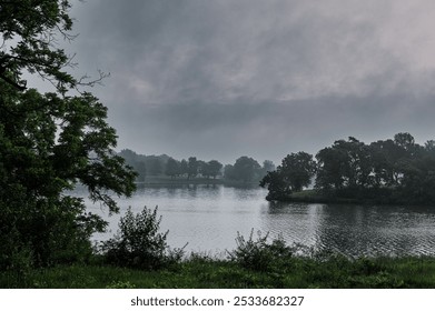 A serene lake surrounded by lush green trees under a misty sky - Powered by Shutterstock