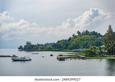 Serene Lake View with Boats, Pier and Lush Green Hills Under a Cloudy Sky - Powered by Shutterstock