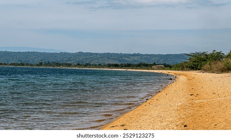 serene lakeshore with a sandy beach, clear blue water, and a mountain range in the background. - Powered by Shutterstock