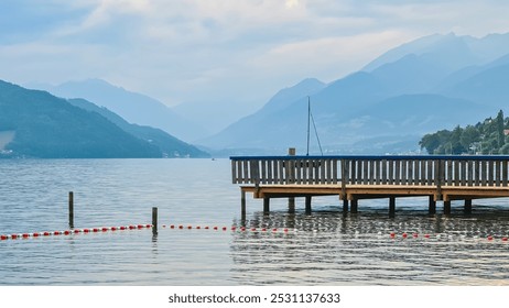 Serene lakeside scene with wooden pier extending into the calm waters of Lake Millstatt, Carintha, Austria. Majestic mountains rise from the horizon shrouded in mist. Wanderlust Austrian Alps - Powered by Shutterstock