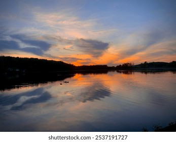 a serene lakeside sunset with vibrant hues of orange, pink, and blue streaking across the sky. Wispy clouds reflect softly on the calm water, adding depth and tranquility to the scene. - Powered by Shutterstock