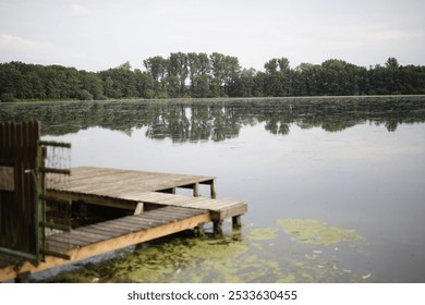 A serene lakeside view with a wooden dock extending into the calm water, surrounded by lush green trees under a cloudy sky. - Powered by Shutterstock