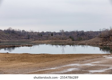 A serene landscape captures a still pond surrounded by bare trees, reflecting the calm of early spring. The overcast sky enhances the peaceful atmosphere of the natural scene. - Powered by Shutterstock