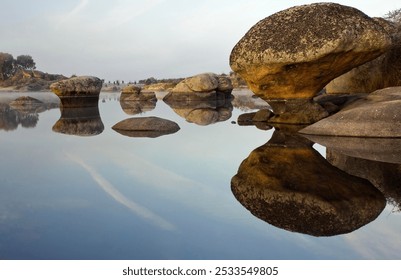 A serene landscape featuring large rock formations reflecting in still water under a clear sky. - Powered by Shutterstock