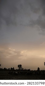 A serene landscape view featuring a dramatic cloudy sky during sunset over a rural horizon with silhouettes of trees.