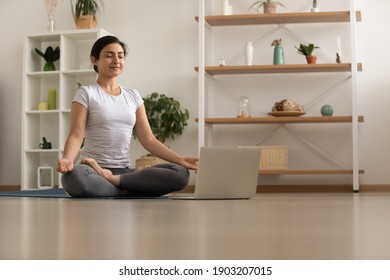 Serene Millennial Mixed Race Woman Engaged In Yoga Practice Breath Deep Feel Comfort Harmony. Tranquil Inspired Young Indian Lady Sit By Laptop On Floor At Lotus Asana Meditate To Reach Peace Of Mind