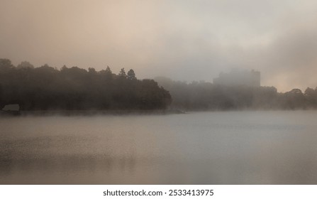 A serene misty morning landscape over a calm lake with soft sunlight breaking through the fog - Powered by Shutterstock