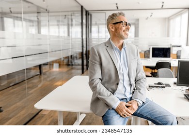 Serene modern middle aged businessman in formal wear leaned on the desk looking away, inspired and calm mature business owner at the office, confident grey-haired man in relaxed pose - Shutterstock ID 2348547135