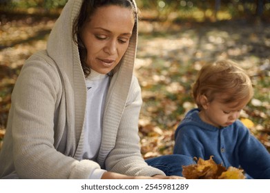 A serene moment capturing a mother and her child spending quality time together outdoors. Surrounded by colorful autumn leaves, they share a quiet, intimate bond, reflecting warmth and care. - Powered by Shutterstock