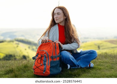 A serene moment of a young woman sitting on a hilltop with a colorful backpack during a peaceful afternoon hike - Powered by Shutterstock